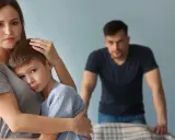 Smutna kobieta tuli syna, podczas gdy partner patrzy z dystansu. Trudno jej zaakceptować dziecko partnera.