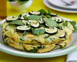 Deliciosa tortilla de calabacín apilada, adornada con rodajas de calabacín, espinacas y perejil fresco.