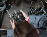 Mechanik trzyma wałki z zębatkami, przygotowując części samochodowe do wysyłki.
