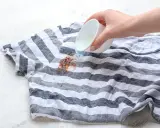 Jak usunąć plamy z czekolady? Płynny środek wylewany na brudny, pasiasty t-shirt.