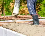 Betoniarz w gumowcach zalewa zbrojenie, wybierając odpowiedni **beton na fundament**.