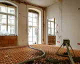 Installation d'un chauffage au sol ancienne génération, avec tuyaux orange et une machine de projection de chape.