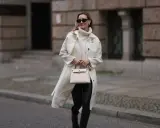 Elegancka kobieta w kremowym płaszczu, golfie i skórzanych legginsach, z beżową torebką. Stylowe skórzane legginsy stylizacje.