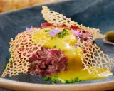 Delicioso steak tartar con huevo crudo, crujiente de queso y pepinillos. Una receta para disfrutar.