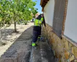 Trabajador con equipo de protección realiza trabajos de inyección de cemento en la base de una pared exterior, rodeado de vegetación.