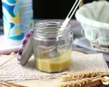 Un bocal de vinaigrette maison, prêt à assaisonner une salade fraîche. Une cuillère repose dans le mélange jaune pâle.