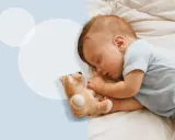 Słodki, 2 miesięczne dziecko śpi spokojnie obok swojego pluszowego misia na białej pościeli.