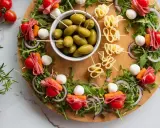 Okrągła deska z 4 wypróbowanymi sałatkami na patyczkach: pomidorki, salami, kulki mozzarelli, marchewka, rukola i oliwki.
