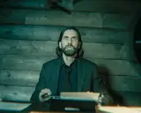 Alan Wake 2: un hombre con barba y pelo largo, con expresión de sorpresa, sentado frente a una máquina de escribir en una habitación de madera.