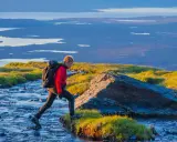 Vandrare korsar en bäck i Abisko, med Kebnekaise-massivet i bakgrunden.