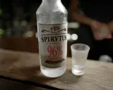 Spirytus 96% – alkohol, który ma najwięcej procent. Butelka i kieliszek na drewnianym blacie.