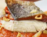 Bacalao a la riojana con piel crujiente, pimientos y ajo frito, servido sobre una cama de salsa de tomate.