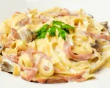 Tagliatelle z szynką i pieczarkami w kremowym sosie, ozdobione natką pietruszki. Pyszny makaron z mozzarellą w roli głównej.