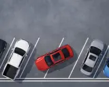 Czerwony samochód zajmuje dwa miejsca parkingowe, blokując sąsiednie pojazdy. Obok stoją czarny, biały pickup, srebrny i niebieski.