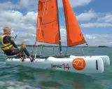 Deux jeunes garçons naviguent sur un petit voilier 2 places, leurs voiles oranges gonflées par le vent sous un ciel bleu et nuageux.