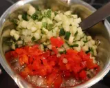 Finhackad gurka och röd paprika i en kastrull, redo för ett bostongurka recept. En sked vilar i blandningen.
