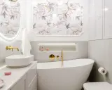 Elegancka, biała łazienka glamour z wolnostojącą wanną, złotymi bateriami i tapetą w kwiaty.