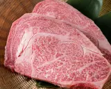 Dos cortes de carne japonesa cara, con marmoleado intenso, reposan sobre hojas verdes en una cesta de mimbre.
