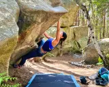 Kobieta wspina się po skale w lesie, doświadczając emocji związanych z boulderingiem w Fontainebleau.
