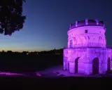 Torre antica illuminata di viola in una magica pink night. L'erba e gli alberi riflettono la luce, creando un'atmosfera surreale.