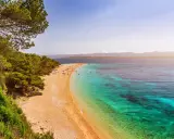 Traumhafter kroatischer Strand mit Pinienwald, goldenem Sand und kristallklarem, türkisfarbenem Wasser. Menschen entspannen sich und baden.