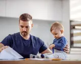 Ojciec pracuje w domu, a dziecko siedzi obok, bawiąc się długopisem. To obraz codziennych kontaktów z dzieckiem w miejscu zamieszkania matki.