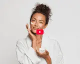 Donna sorridente applica crema viso, un gesto di skincare semplice per una pelle radiosa.