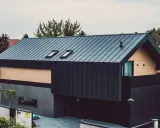 Nowoczesny dom z ciemną elewacją z blachy trapezowej, drewnianymi panelami i dwoma oknami dachowymi.