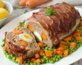 Ein saftiger falscher Hase, umwickelt mit Speck, gefüllt mit Eiern und Karotten, serviert auf Erbsen und Karotten.