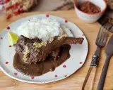 Un delicioso conejo guisado en mole oscuro, servido con arroz blanco y una rodaja de limón.