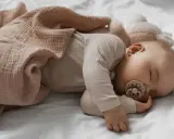 Dolce neonato di 3 mesi dorme sereno, avvolto in una copertina rosa cipria, con un ciuccio in bocca.