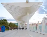 Passeggiata moderna al malaga porto, con palme, una nave bianca e un cielo nuvoloso.