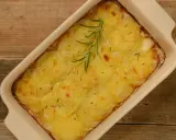 En ugnsform med gyllene, tunna potatisskivor, en klassisk pommes anna, toppad med en rosmarinkvist.