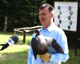 Mężczyzna w błękitnej koszuli prezentuje sokoła na rękawicy. Obok mikrofon TVN24.