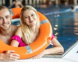 Uśmiechnięta para w basenie, trzymająca koło ratunkowe. Idealny weekend z przyjaciółką, pełen relaksu i zabawy w wodzie.