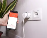 Smart wtyczka w gniazdku i smartfon z wykresem pokazującym monitoring zużycia energii.