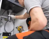 Plombier en action pour déboucher une canalisation sous un évier. Outils à portée de main pour résoudre le problème.