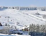 Ośnieżony stok narciarski z narciarzami, wyciągami i budynkami w tle.