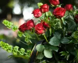 Wieniec pogrzebowy dla brata: bukiet czerwonych róż i zielonych liści, ozdobiony czarną wstęgą ze złotym brzegiem.