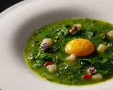 Un uovo dorato in una crema verde brillante, con cubetti bianchi e fiori viola. Un'idea di cosa mangiare a Viterbo, un piatto raffinato.