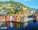 Kolorowe domy nad wodą w Bergen, idealne na norwegia zwiedzanie. W tle wzgórza porośnięte drzewami.