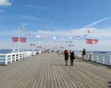 Spacer po najdłuższym molo w Polsce. Ludzie przechadzają się pod biało-czerwonymi flagami i błękitnym niebem.