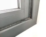 Gotas de lluvia resbalan por el marco de una ventana gris, dejando un rastro húmedo.