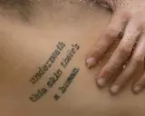 Tatuaż z cytatem "Underneath this skin there's a human" na skórze, z kroplami wody.