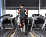 Mann mit Kopfhörern absolviert ein intensives Laufband Training in einem modernen Fitnessstudio.