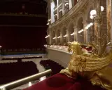 Interno del Teatro Galli di Rimini, con poltrone rosse, palchi dorati e una sfinge alata in primo piano.