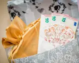 Elegancki sposób na to, jak zapakować pieniądze na ślub: banknoty 10 euro w ozdobnej kopercie, w złotej sakiewce, w ozdobnej torbie.