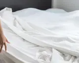 Dłoń kobiety sięga do białej pościeli, przygotowując się do zadania, jak założyć poszewkę na kołdrę.