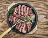 Una succulenta bistecca fiorentina affettata, guarnita con rosmarino, pronta per essere gustata.