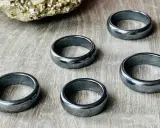 Pięć błyszczących, ciemnoszarych pierścionków z hematytu na drewnianym tle. Jak rozpoznać hematyt? Po jego metalicznym połysku i ciężarze.